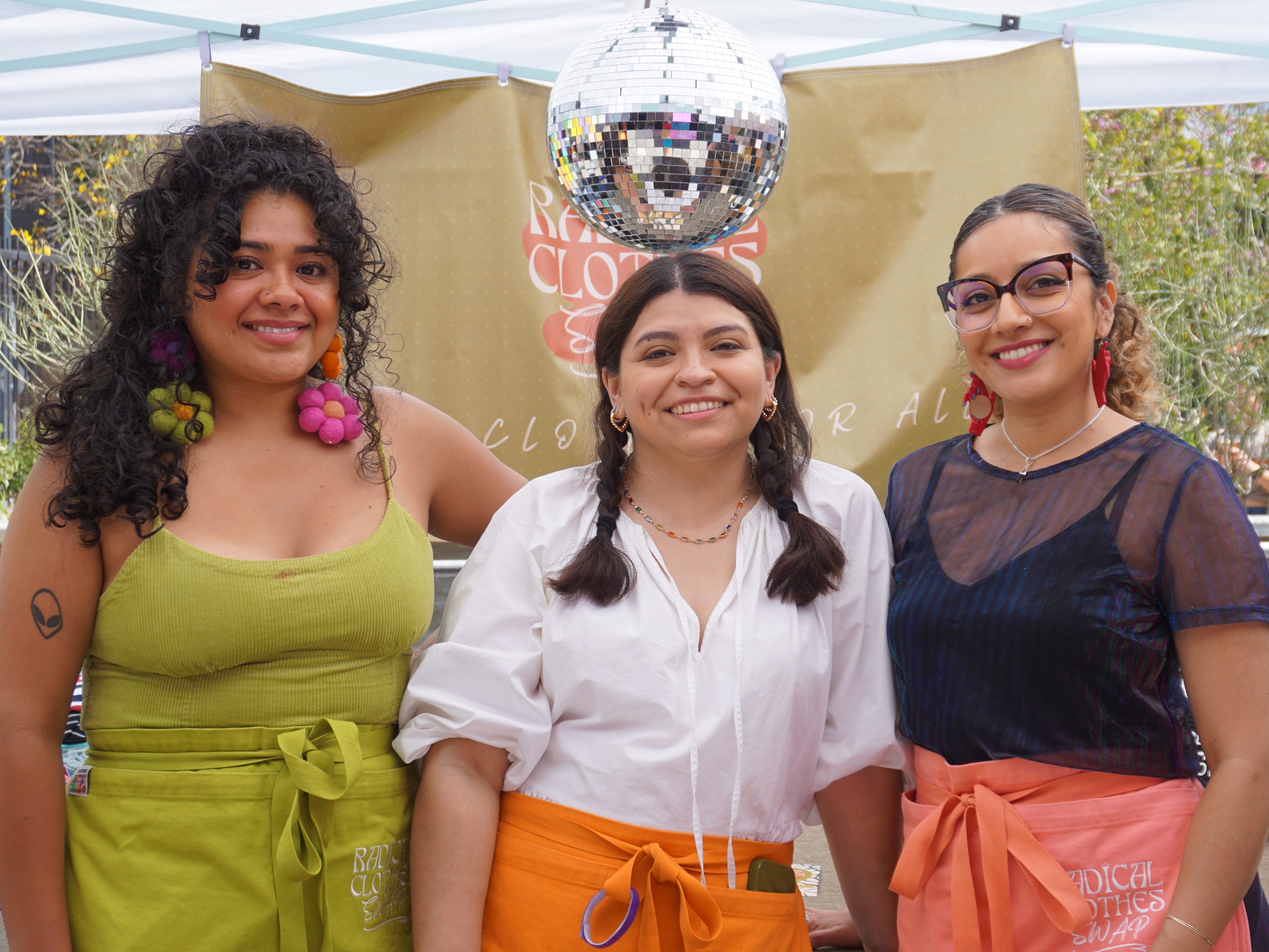 Jannine, Enri, and Nicole stand smiling under a disco ball at one of their most successful clothing swaps.
